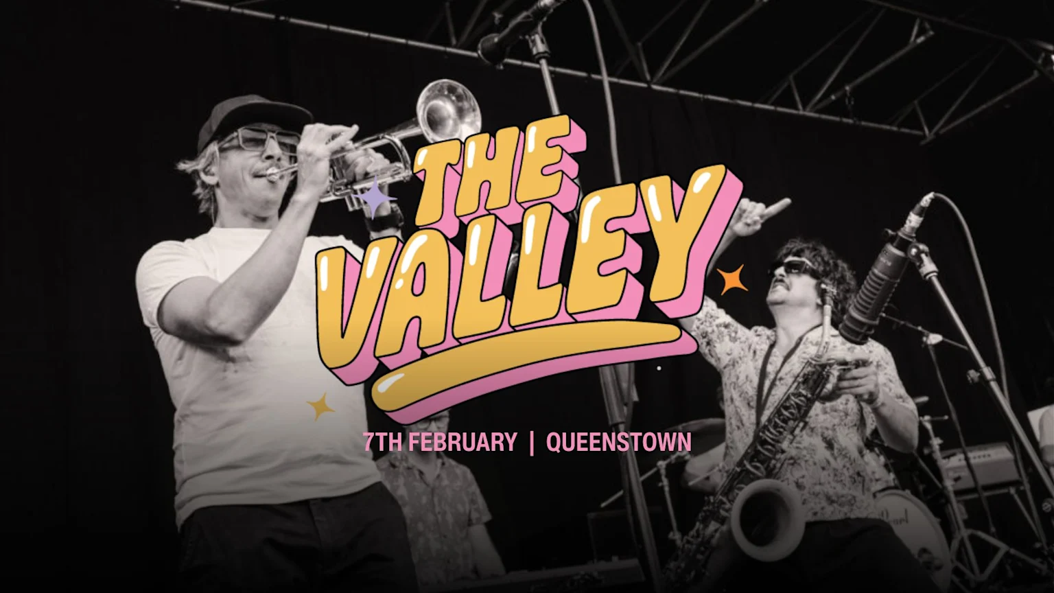 Black and white photo of two musicians on stage, one playing trumpet and another saxophone, with "THE VALLEY" in colorful bubble text overlayed, and "7TH FEBRUARY | QUEENSTOWN" below.