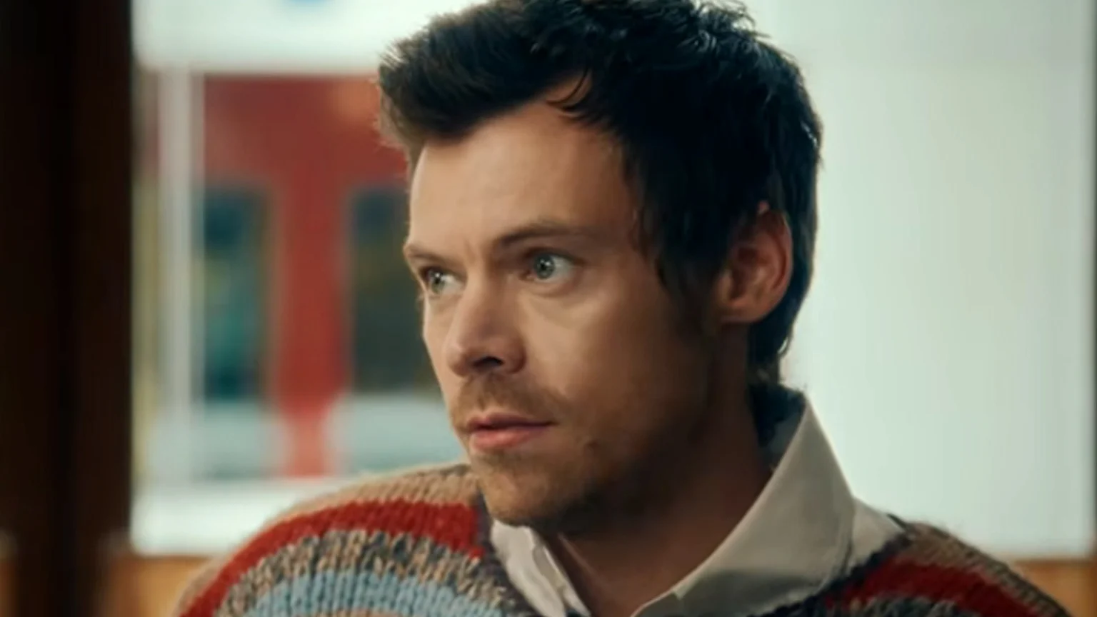 Harry Styles with messy hair and light stubble, wearing a pinstripe suit, light blue striped shirt, and striped tie, against a BRIT Awards 2026 backdrop.