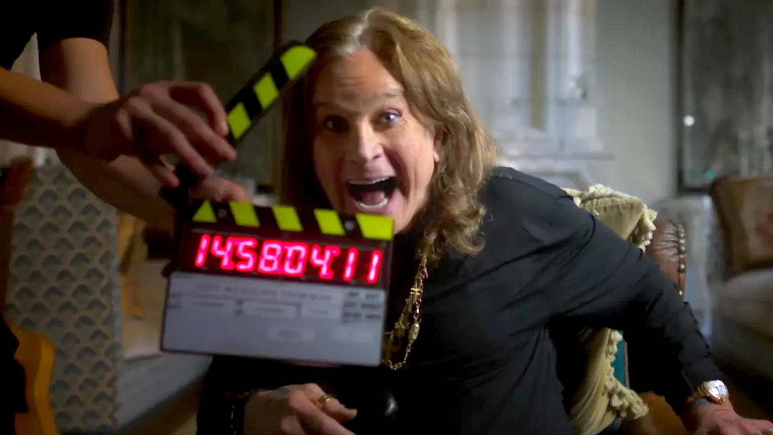 Ozzy Osbourne smiling behind a clapper board.