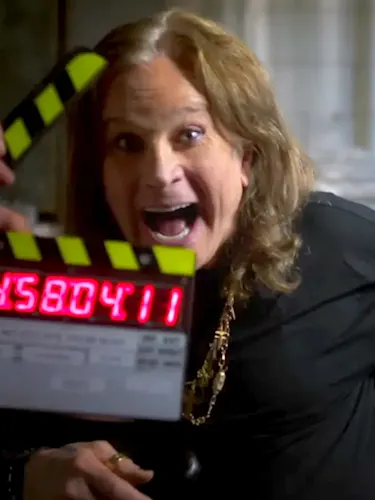 Ozzy Osbourne smiling behind a clapper board.