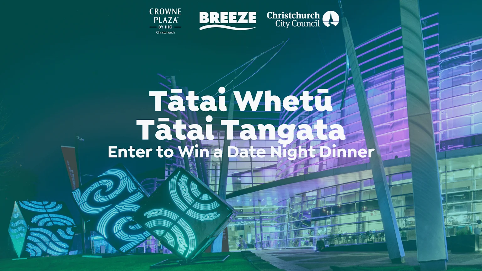 A vibrant night scene featuring a modern building illuminated in purple and large cubic sculptures glowing with blue-green patterns, with text "Tātai Whetū Tātai Tangata" and "Enter to Win a Date Night Dinner."