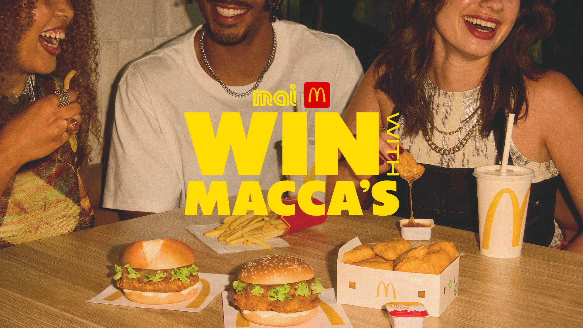 Three adults sitting together having McDonald's. "Win with Macca's" with Mai FM and McDonalds