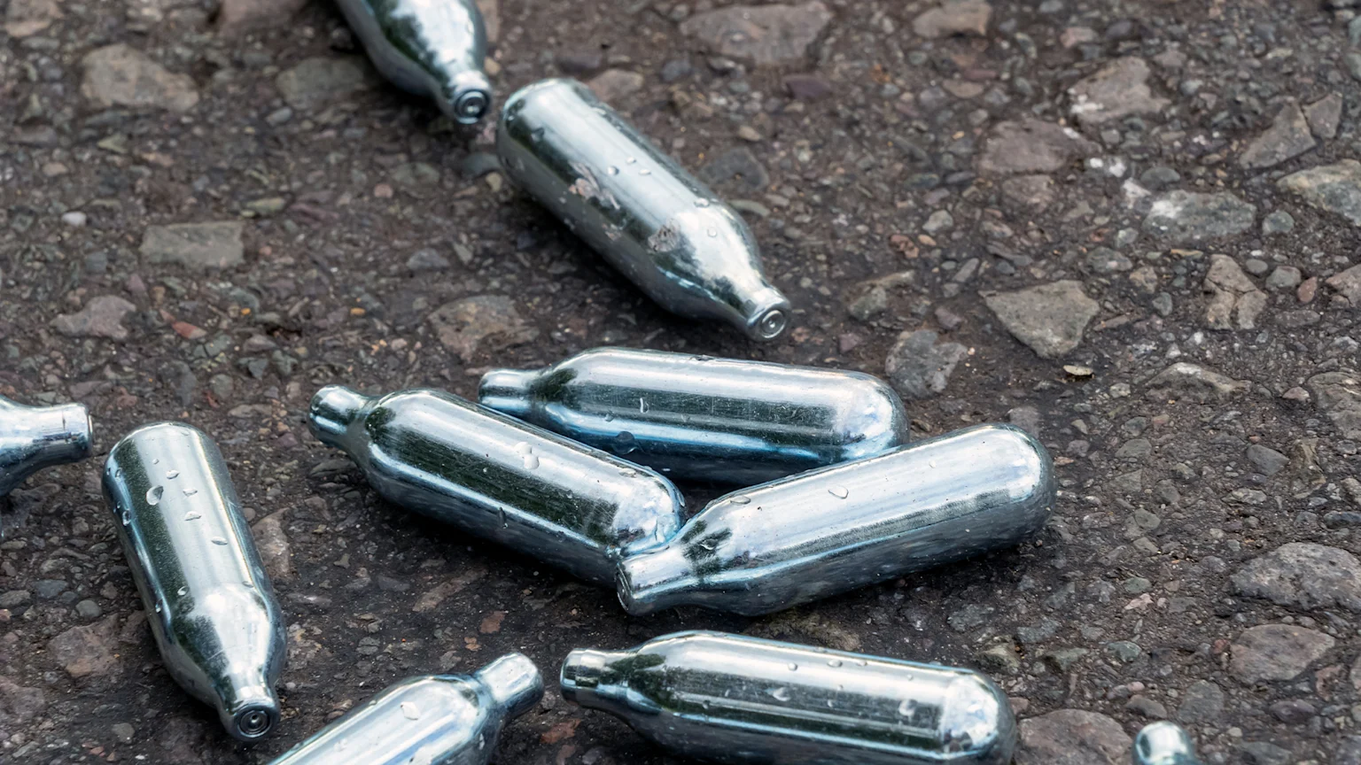 silver nitrous oxide canisters laying on a footpath.
