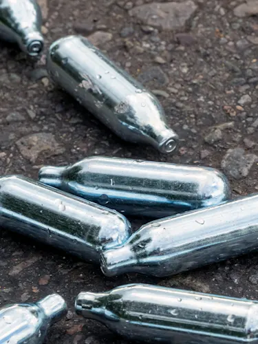 silver nitrous oxide canisters laying on a footpath.