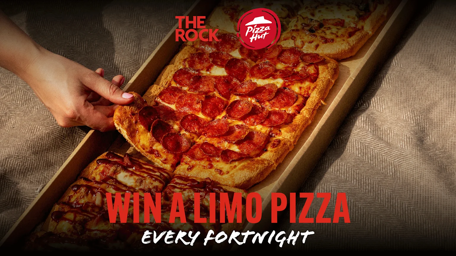 A hand reaches for a slice of a long, rectangular pepperoni pizza, also known as a "Limo Pizza," from a box, with Pizza Hut logos and "Win a Limo Pizza Every Fortnight" text.