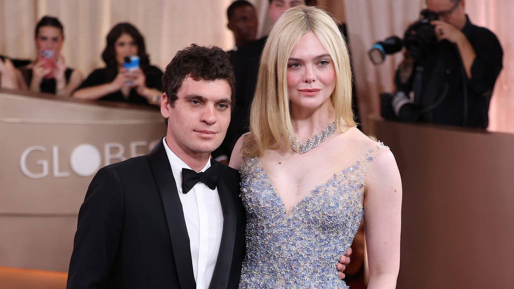 Elle Fanning in a light blue beaded gown and Gus Wenner in a tuxedo with his arm around her, pose at an event with "GLOBE" visible in the background.