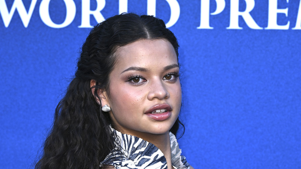 Catherine Laga'aia, a young woman with dark curly hair, light makeup, and a patterned top, looks slightly right against a blue "WORLD PREMIERE" banner.