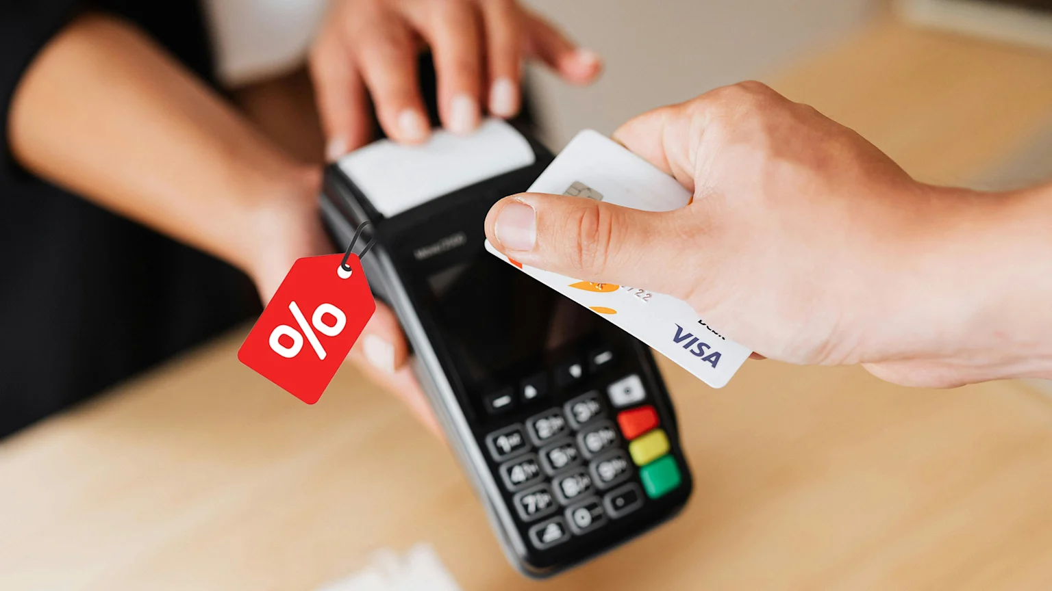 A person is tapping a white Visa credit card on a black point-of-sale terminal, which has a red price tag with a white percent symbol attached to it.