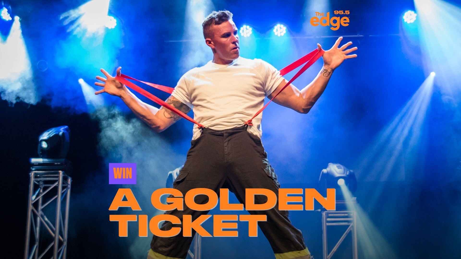 A muscular man in a white t-shirt and dark pants, holding red suspenders, performs on a blue-lit stage with spotlights and smoke; text 'WIN A GOLDEN TICKET' is overlaid.