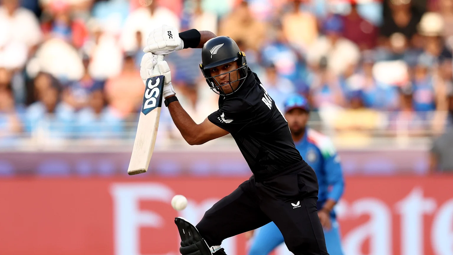 A Blackcaps cricketer wearing a black helmet with a silver fern logo and a black uniform, holding a DSC bat, plays a shot with a white cricket ball near his front leg during a match.
