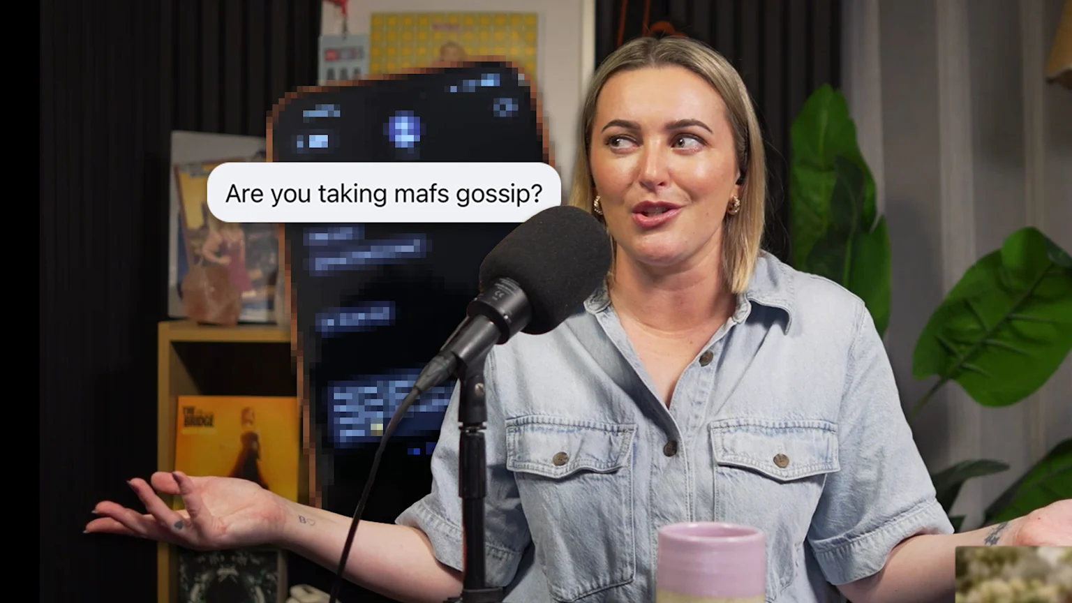 A woman in a denim shirt gestures with her hands as she speaks into a microphone, with a phone screen behind it displaying a text bubble that reads "Are you taking mafs gossip?".