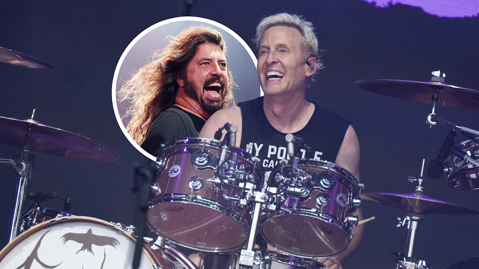 A dynamic concert image showing Chad Smith playing a metallic purple drum set with a black bird design on the bass drum. A circular inset shows Dave Grohl laughing, both under purple stage lighting in an indoor concert environment.