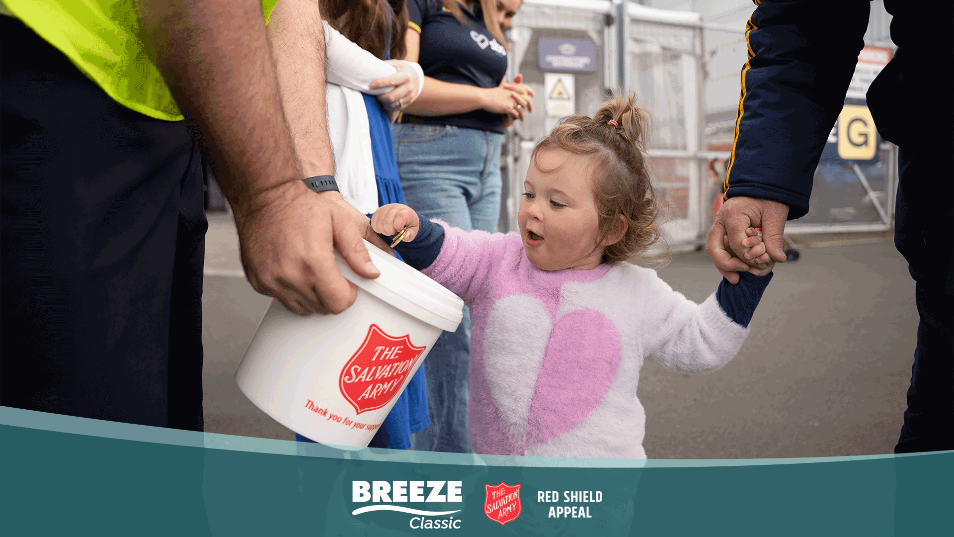 A young child puts a coin into a Salvation Army collection bucket held by an adult, while another adult holds the child's hand, with "Breeze Classic" and "The Salvation Army" logos visible at the bottom.