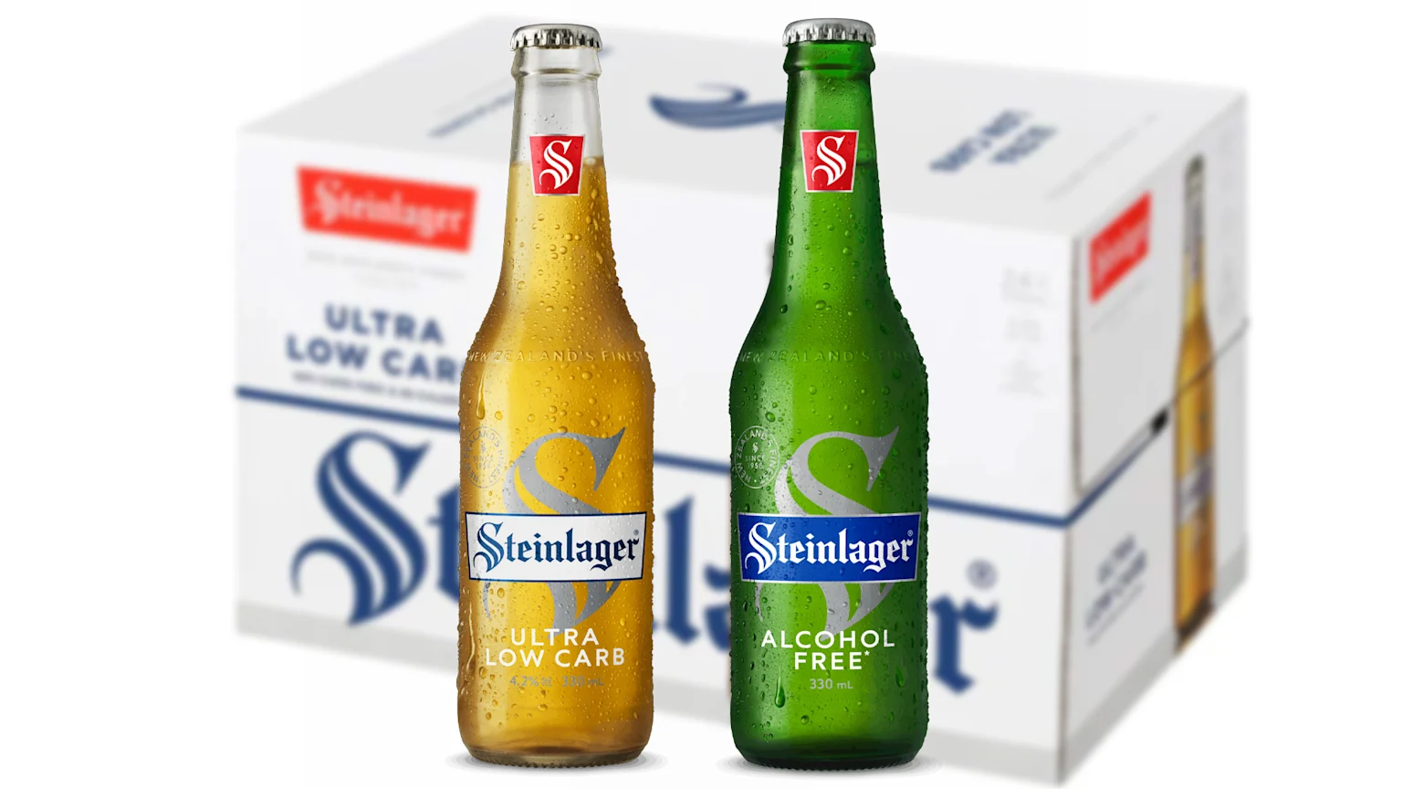 A green Steinlager bottle labeled 'Alcohol Free' stands next to an amber 'Ultra Low Carb' bottle, both covered in condensation, with a blurred carton behind them.