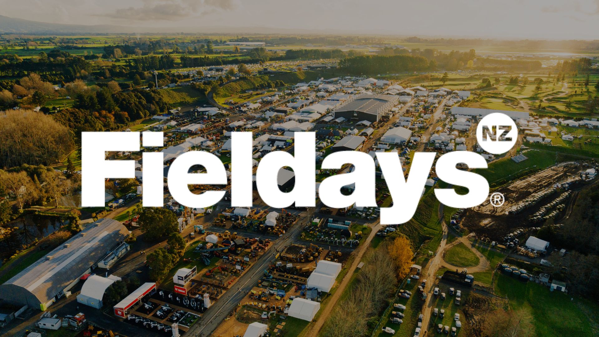 Aerial view of the Fieldays event, showing numerous white tents, machinery displays, and crowds in a large outdoor setting with green fields, overlaid with "Fieldays NZ" logo.