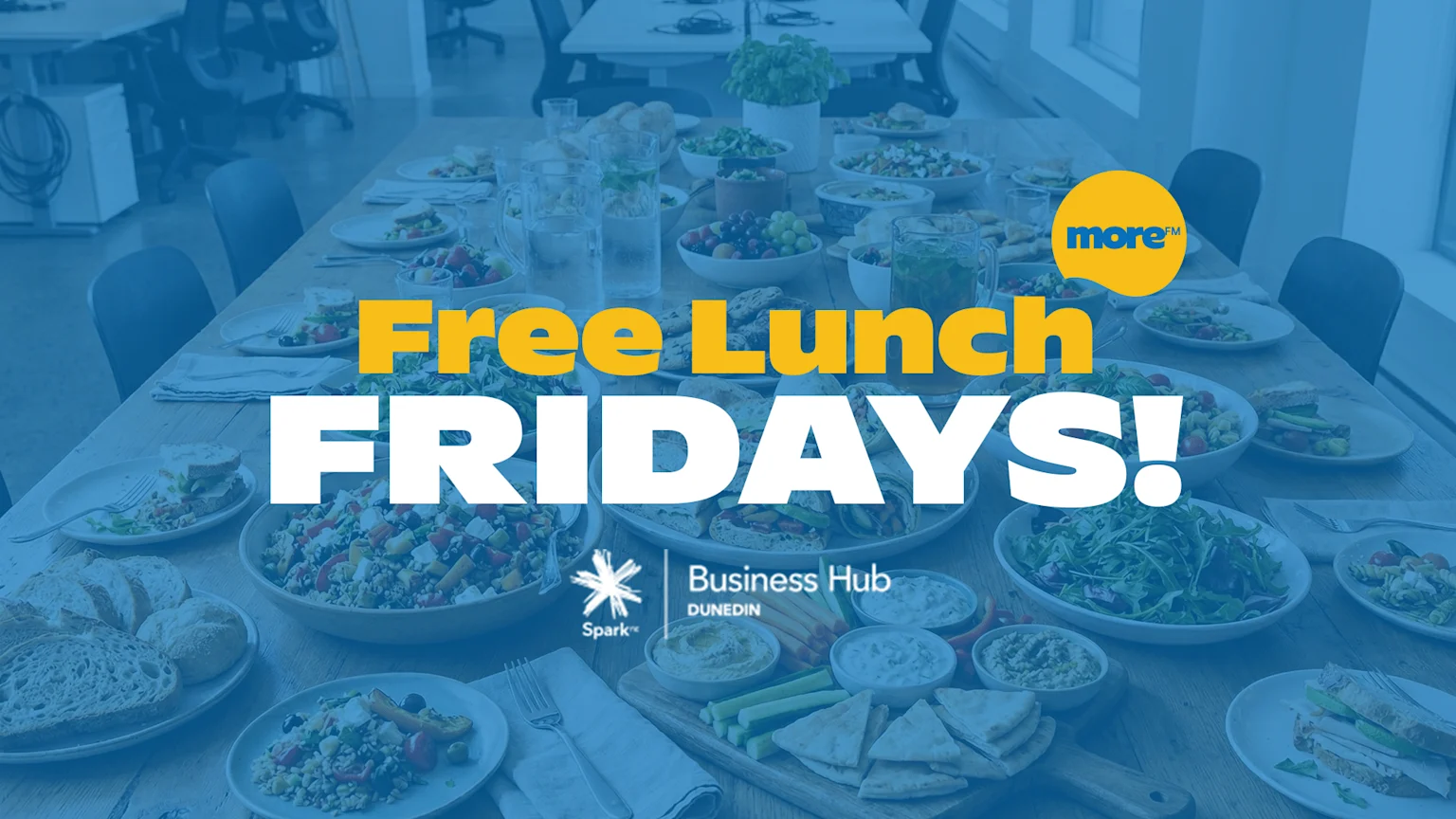 A long table in an office setting is filled with various lunch foods including salads, sandwiches, and fruit, with text overlay "Free Lunch FRIDAYS!" and "more™" and "Spark Business Hub DUNEDIN" logos.