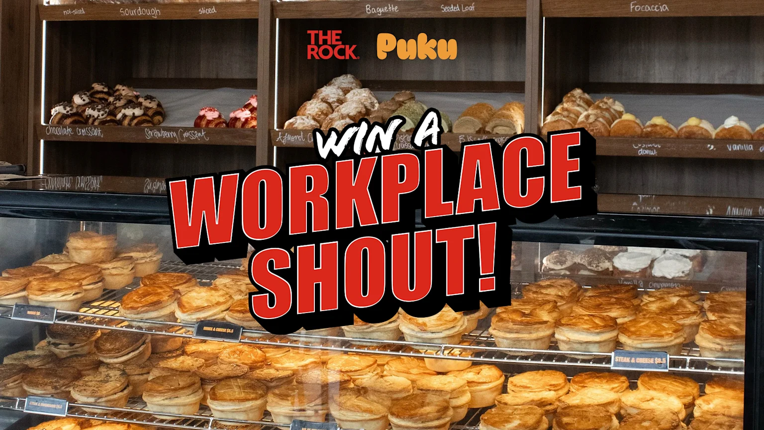 A brightly lit indoor bakery scene showing wooden shelves and a glass display case packed with various baked goods including sourdough and baguettes, croissants, donuts, and savory pies. An overlay promotes a contest with 'WIN A WORKPLACE SHOUT!' text and logos for The Rock and Puku.