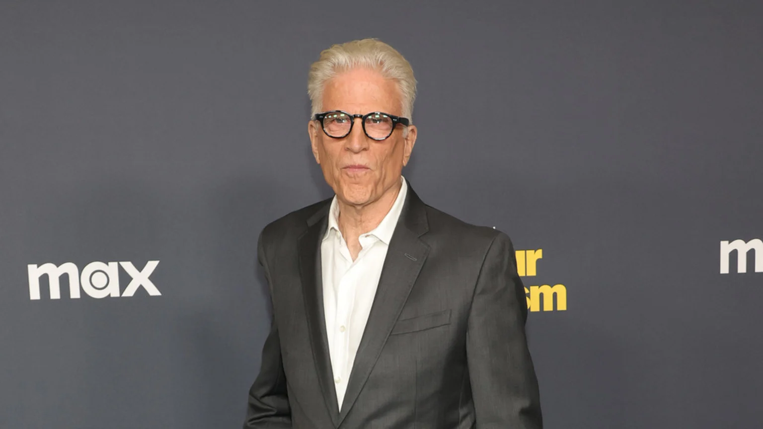 Actor Ted Danson, with white hair and glasses, wears a white shirt and dark suit jacket, standing in front of a dark gray background with "Max" and "Our" logos.