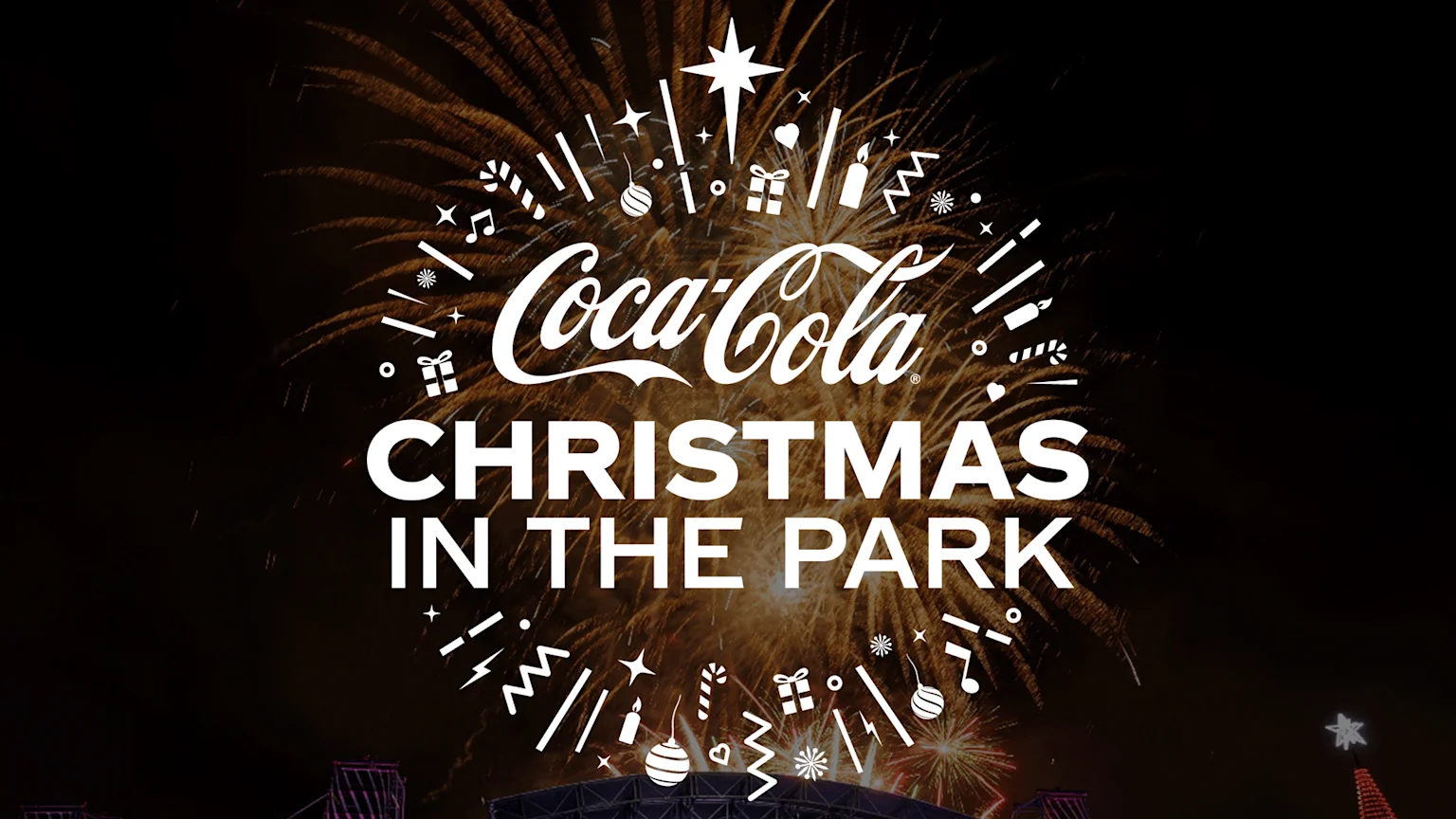White "Coca-Cola Christmas in the Park" text, surrounded by festive icons, is set against a backdrop of golden fireworks.