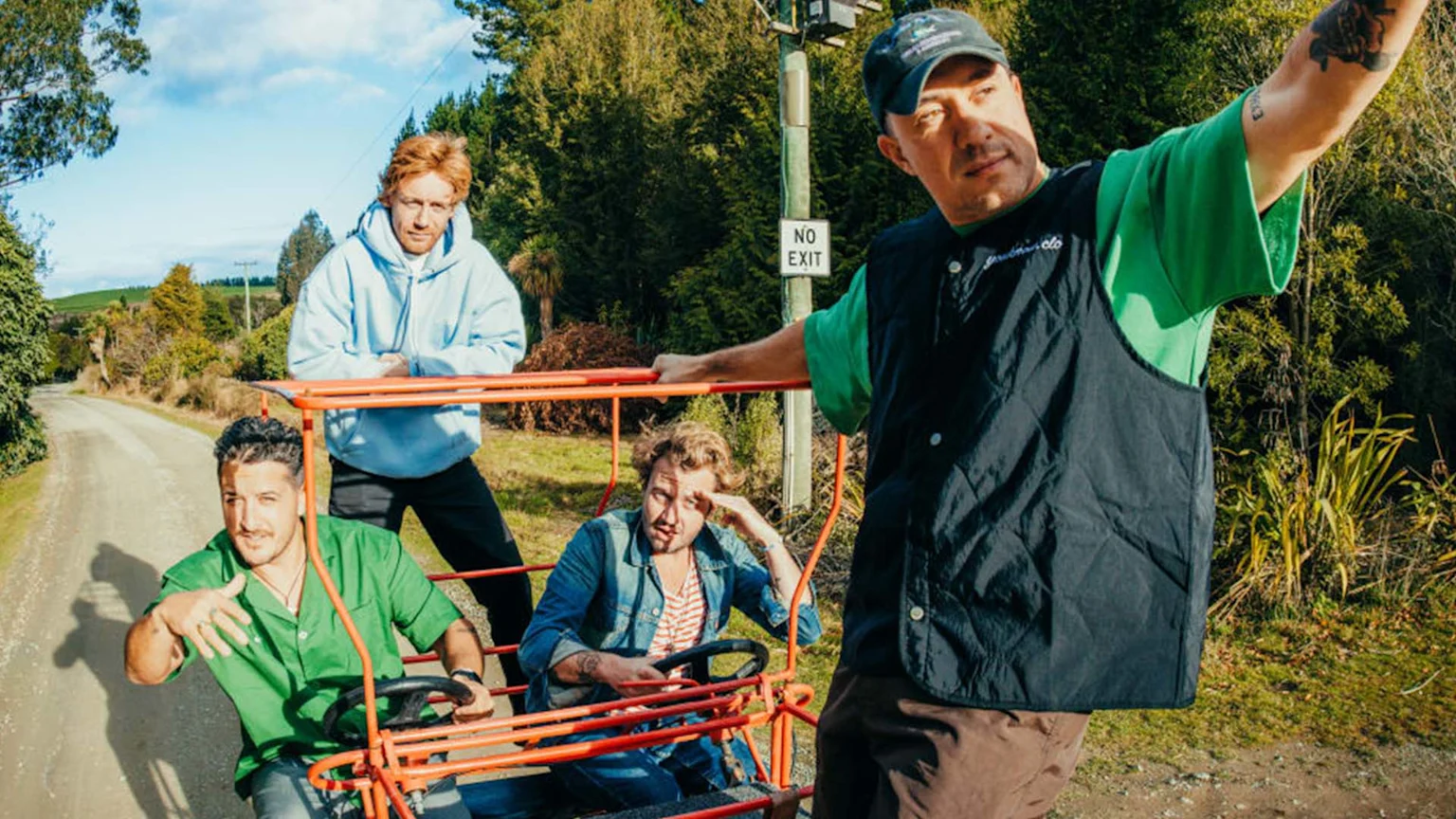 A group of four men pose with a red multi-person pedal vehicle on a rural dirt road, surrounded by trees and a "NO EXIT" sign.