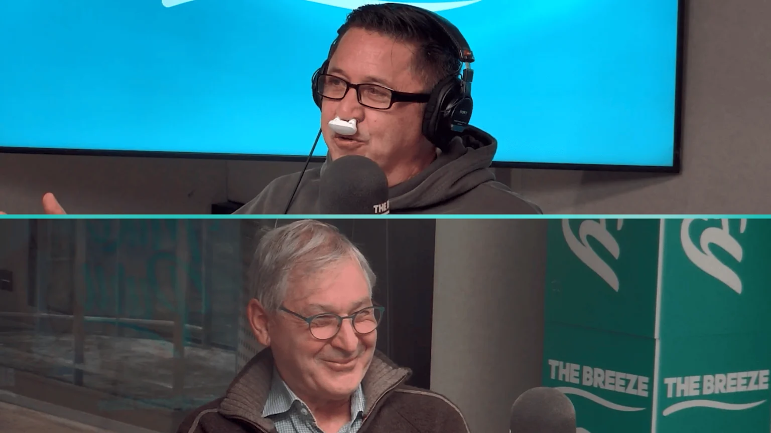 A man with a white nasal device on his nose, headphones, and glasses speaks into a microphone against a blue background, while an older man smiles below him against a green background.