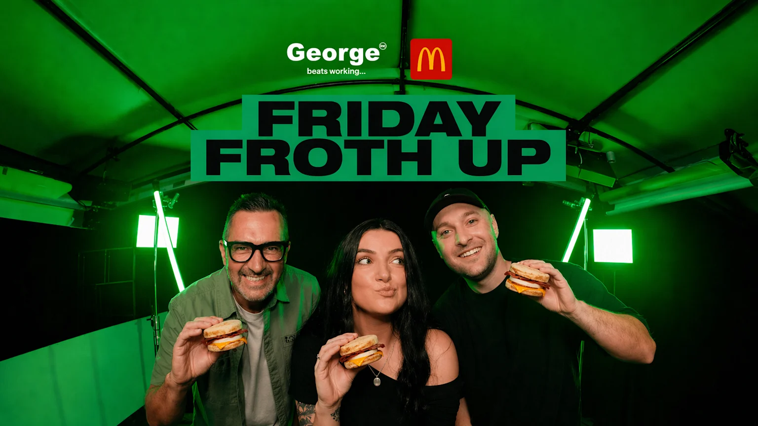 Three smiling people hold McDonald's breakfast sandwiches under a banner reading "FRIDAY FROTH UP," with "George" and the McDonald's logo visible above in a green-lit setting.