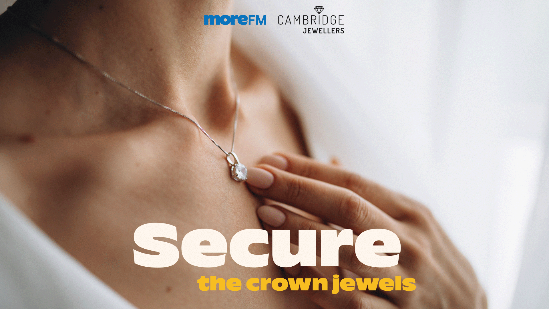 A woman's hand gently touches a solitaire diamond pendant on a silver chain, with "moreFM" and "Cambridge Jewellers" logos, and text "Secure the crown jewels".