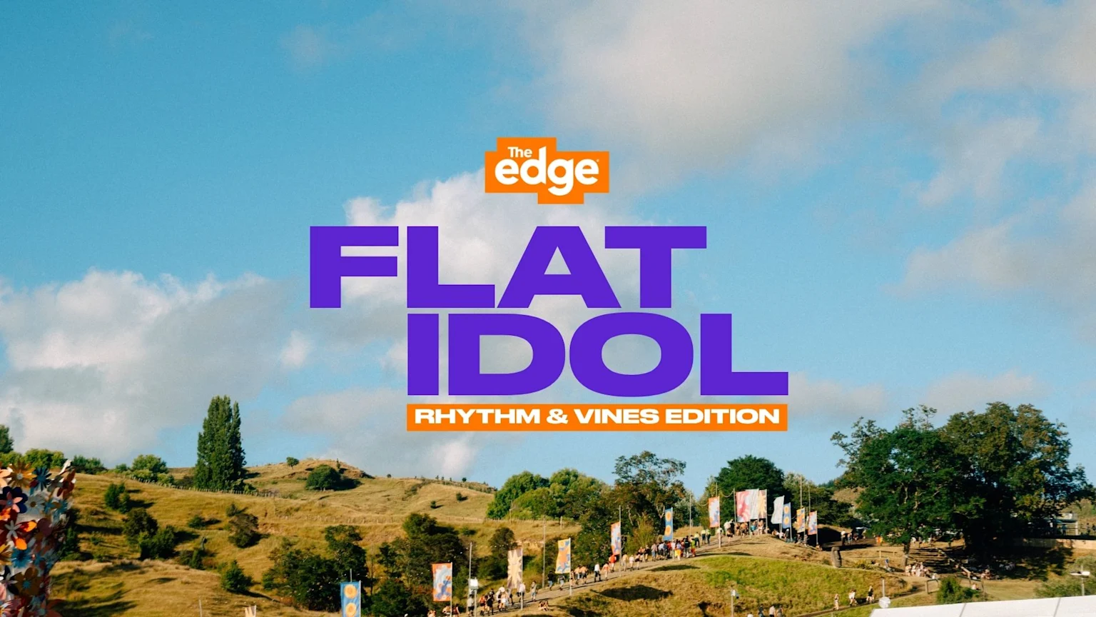 A festival landscape with a winding path, people, trees, and flags under a blue sky, featuring overlay text "The Edge FLAT IDOL RHYTHM & VINES EDITION".