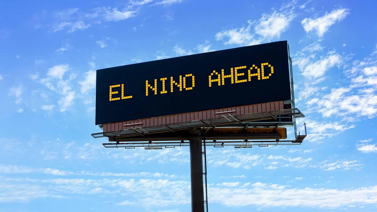A digital billboard displays "EL NINO AHEAD" in yellow, pixelated letters against a bright blue sky with scattered white clouds.