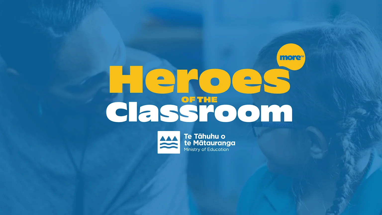 A promotional image with "Heroes OF THE Classroom" in large yellow and white text, featuring the More FM and Ministry of Education logos, over a blurred background of two people.