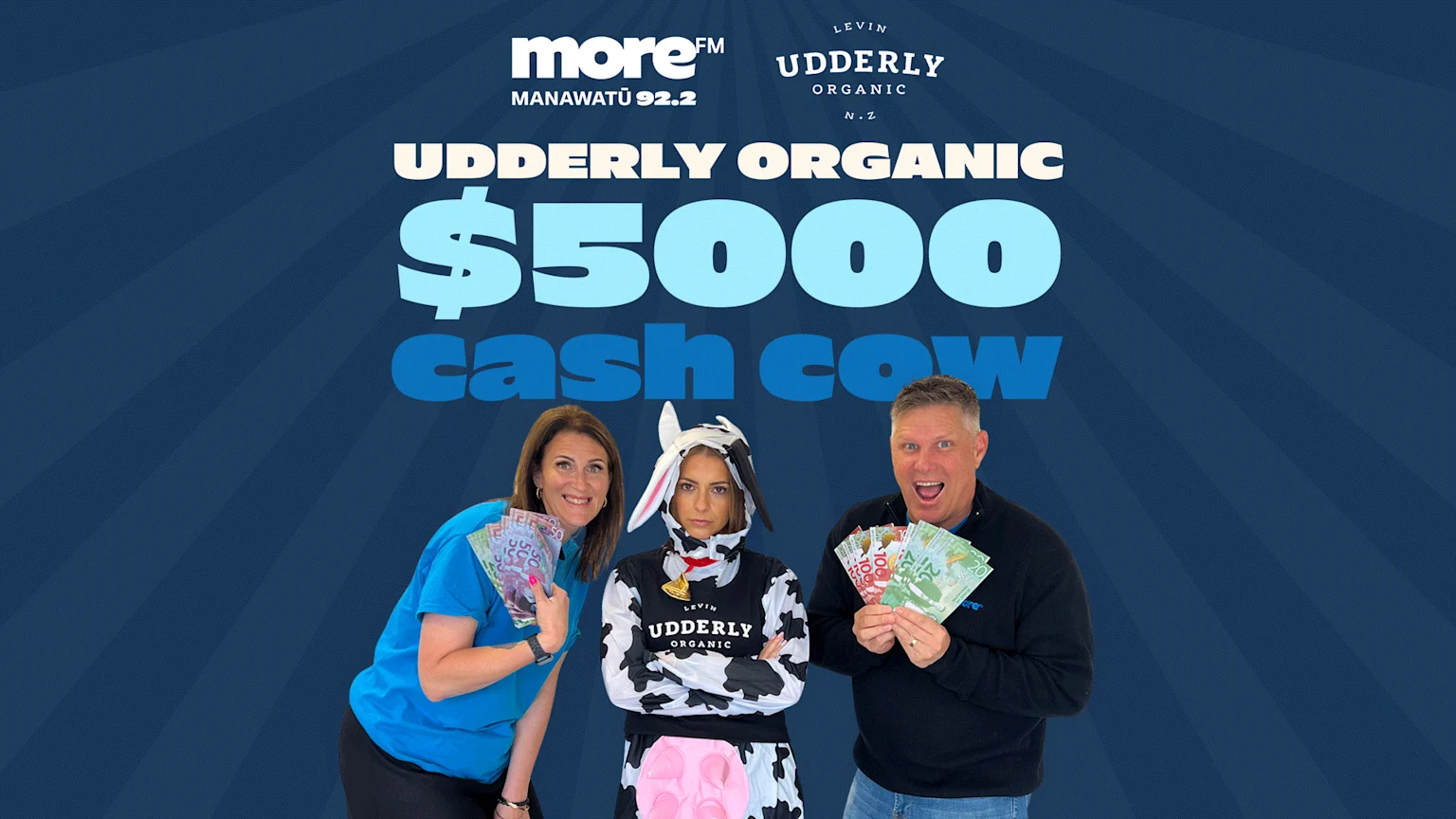 Two smiling people hold cash next to a person in a cow costume, against a blue background with "UDDERLY ORGANIC $5000 cash cow" text.