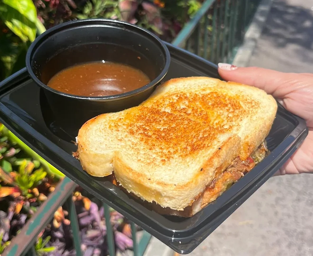A tray holding a birria toastie and consomme.