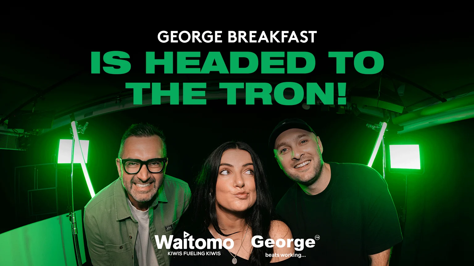 Three hosts (two men, one woman) pose in green light, with the text 'GEORGE BREAKFAST IS HEADED TO THE TRON!' above and sponsor logos 'Waitomo' and 'George' below.