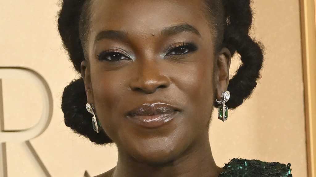 A close-up portrait of actress Wunmi Mosaku smiling slightly, wearing sparkling green drop earrings and a sequined green top, with her dark hair styled in side buns.