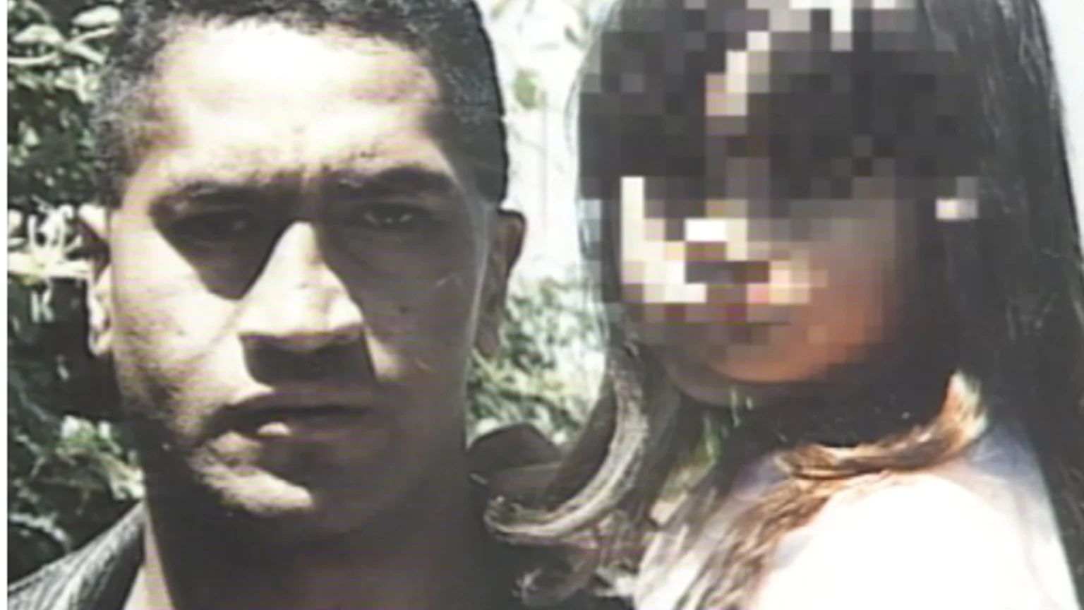 A grainy photo shows a man with dark hair and shadowed eyes looking forward, beside a young girl with long dark hair whose face is heavily pixelated; greenery in the background.