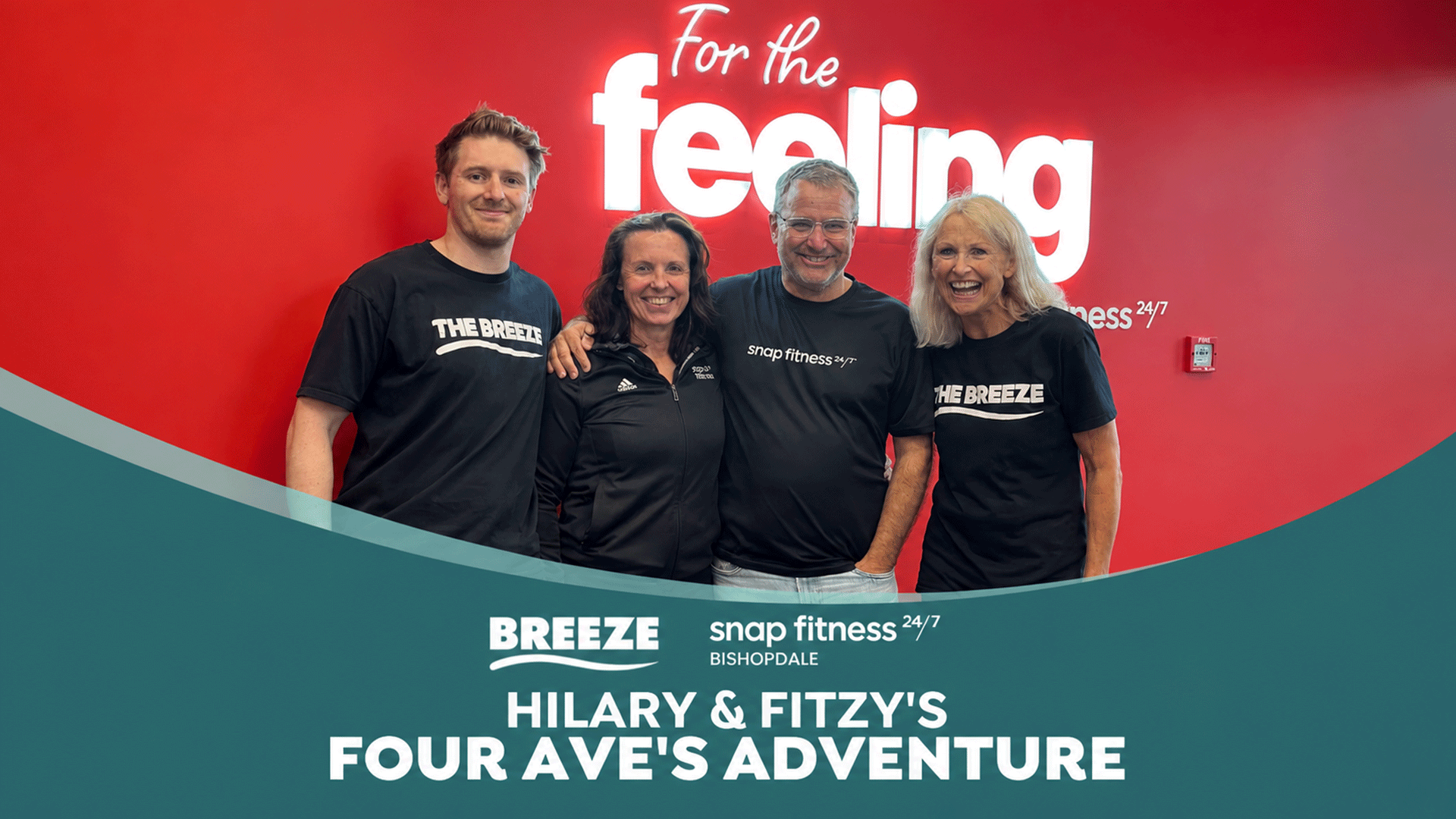 Four smiling people, two men and two women, stand in front of a red wall displaying "For the feeling" and "snap fitness 24/7" text, wearing branded shirts for "THE BREEZE" and "snap fitness".