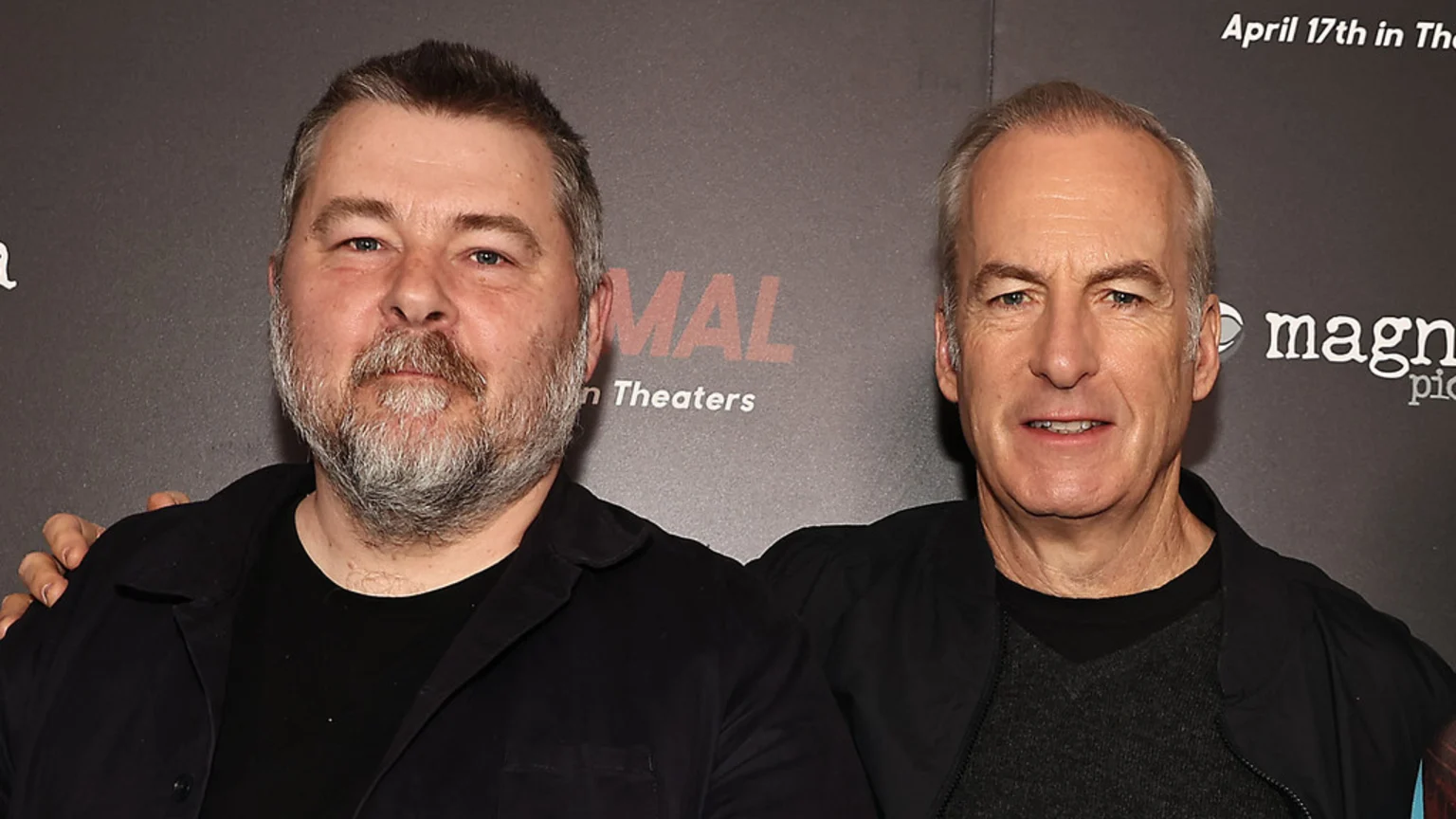 Bob Odenkirk and Ben Wheatley stand side-by-side, smiling at the camera in front of a dark promotional backdrop.
