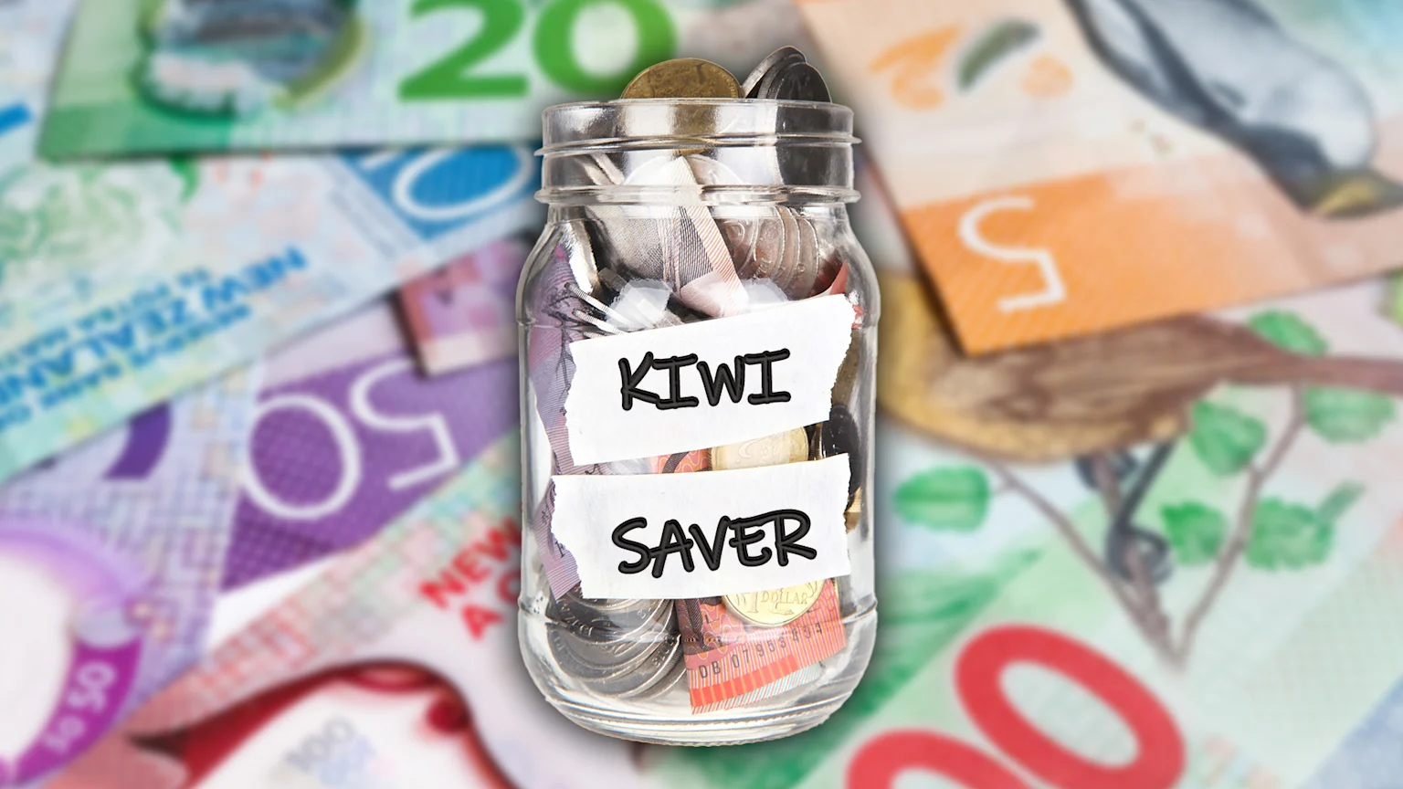 A glass jar labeled "KIWI SAVER" is filled with New Zealand coins and banknotes, set against a blurred background of various New Zealand currency denominations.