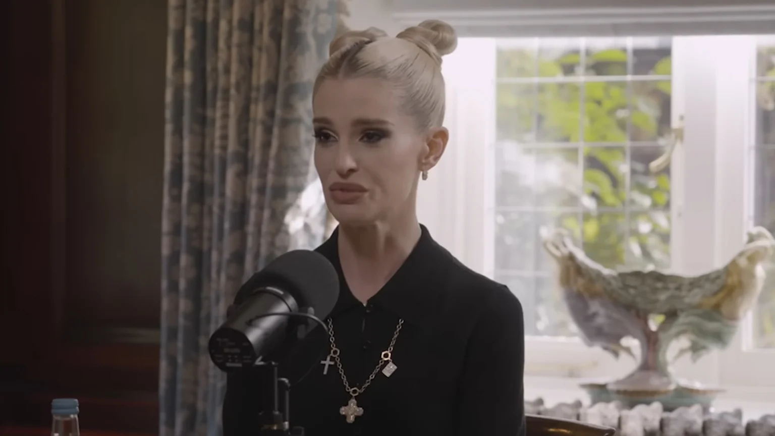 A picture of Kelly Osbourne talking into a microphone on a podcast, with an emotional look on her face.