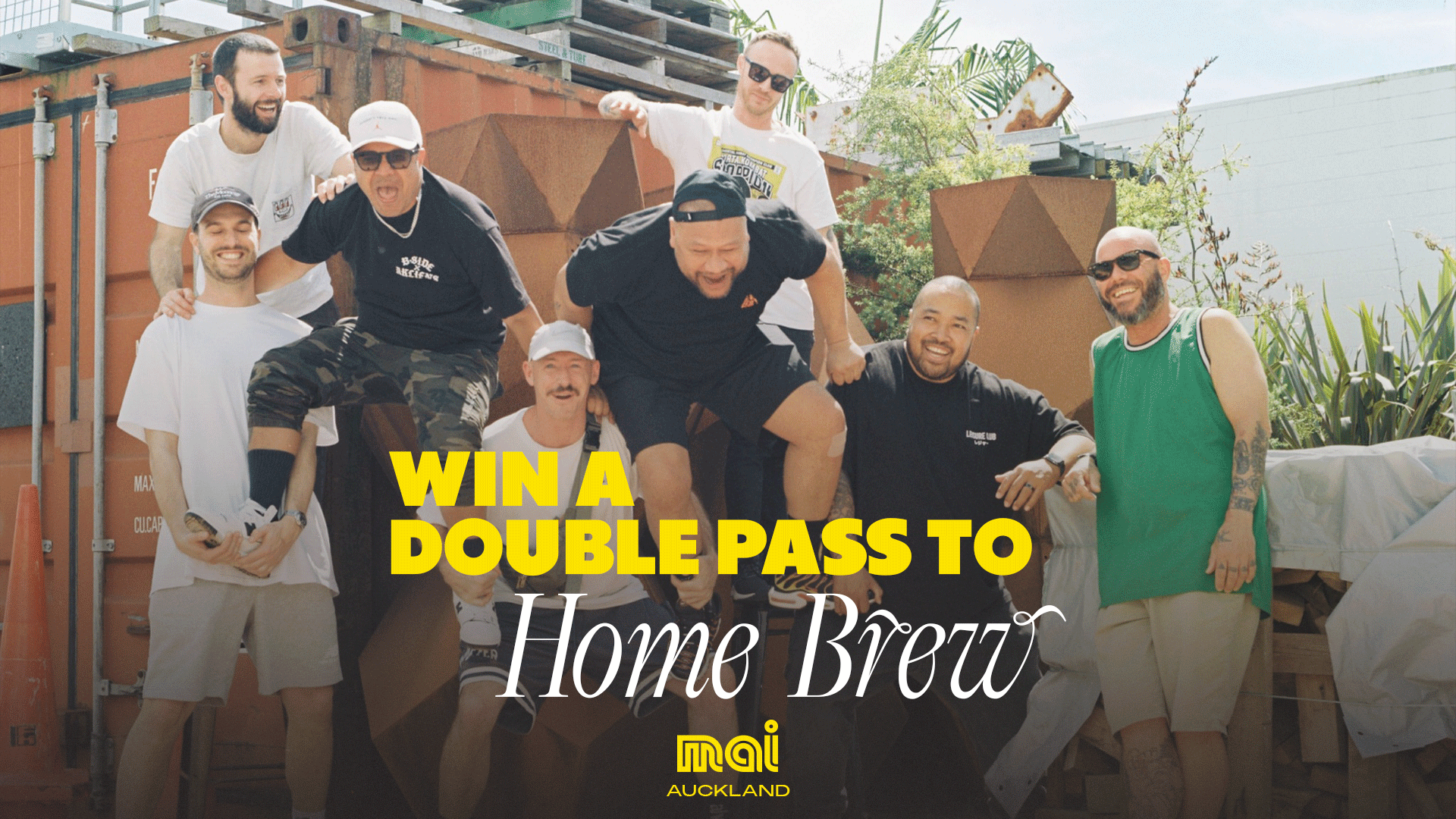 Eight diverse men smile playfully in a dynamic group pose outdoors, with shipping containers and plants in the background.