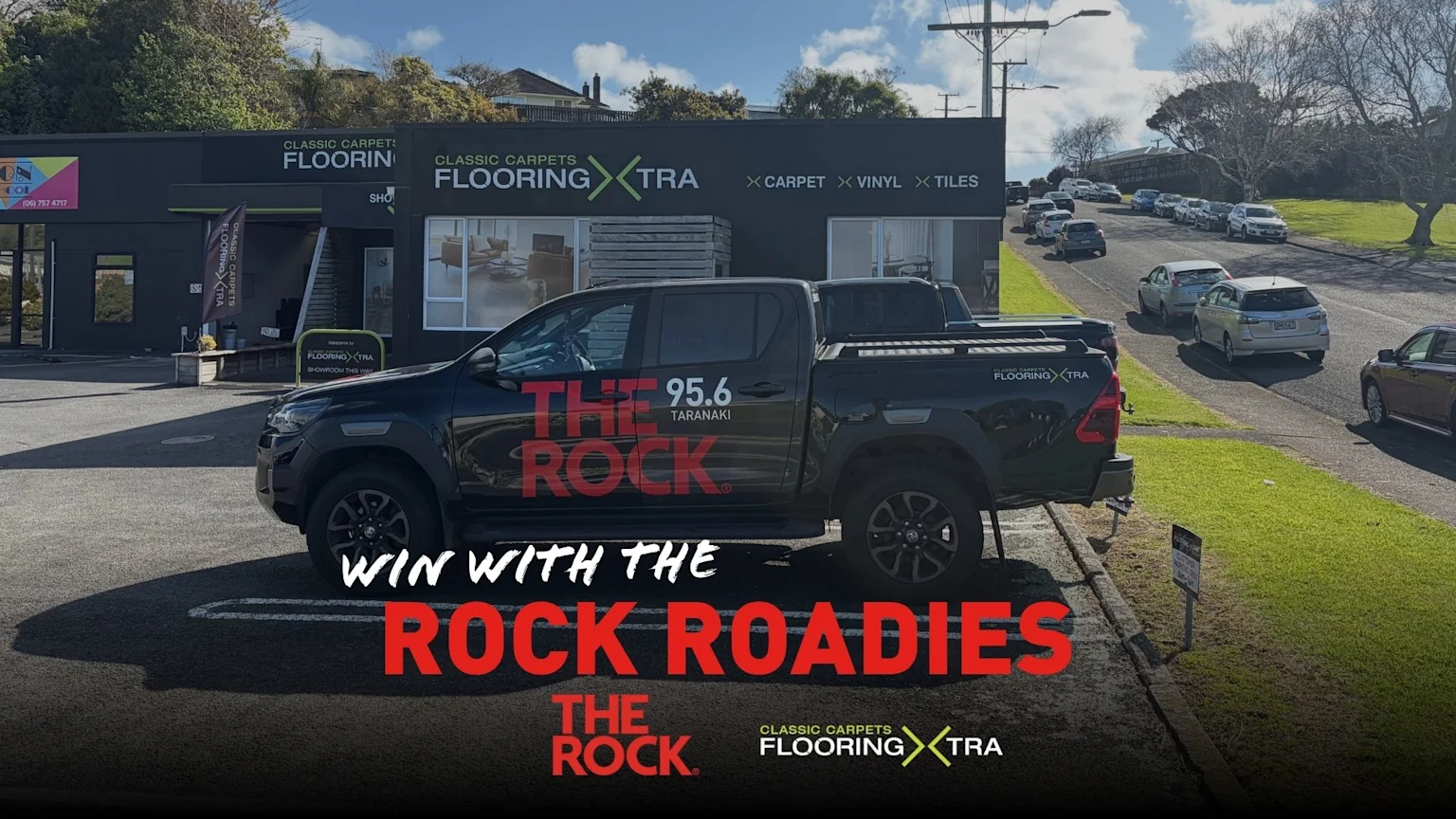A black pickup truck branded "The Rock 95.6 Taranaki" is parked outside "Classic Carpets Flooring Xtra" store, with "Win with The Rock Roadies" text overlay.