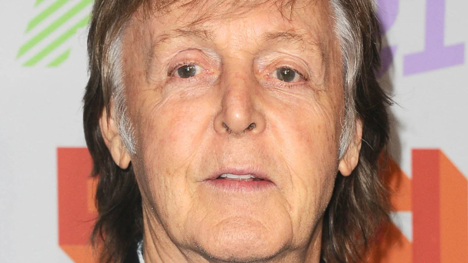 A close-up portrait of Paul McCartney, an older man with light brown and grey hair and a wrinkled face, looking directly forward.