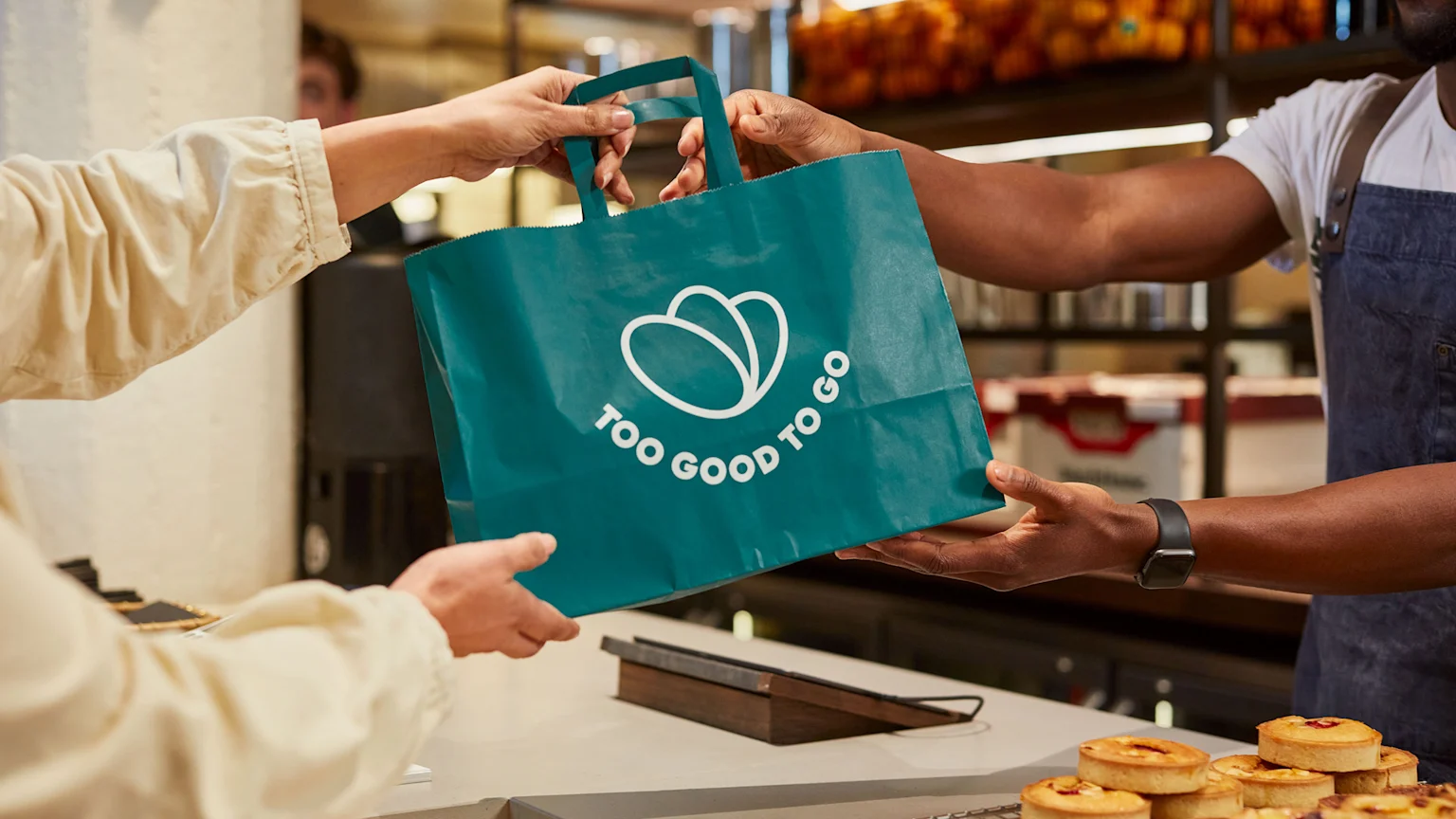 Hands exchanging Too Good To Go bag in a bakery.