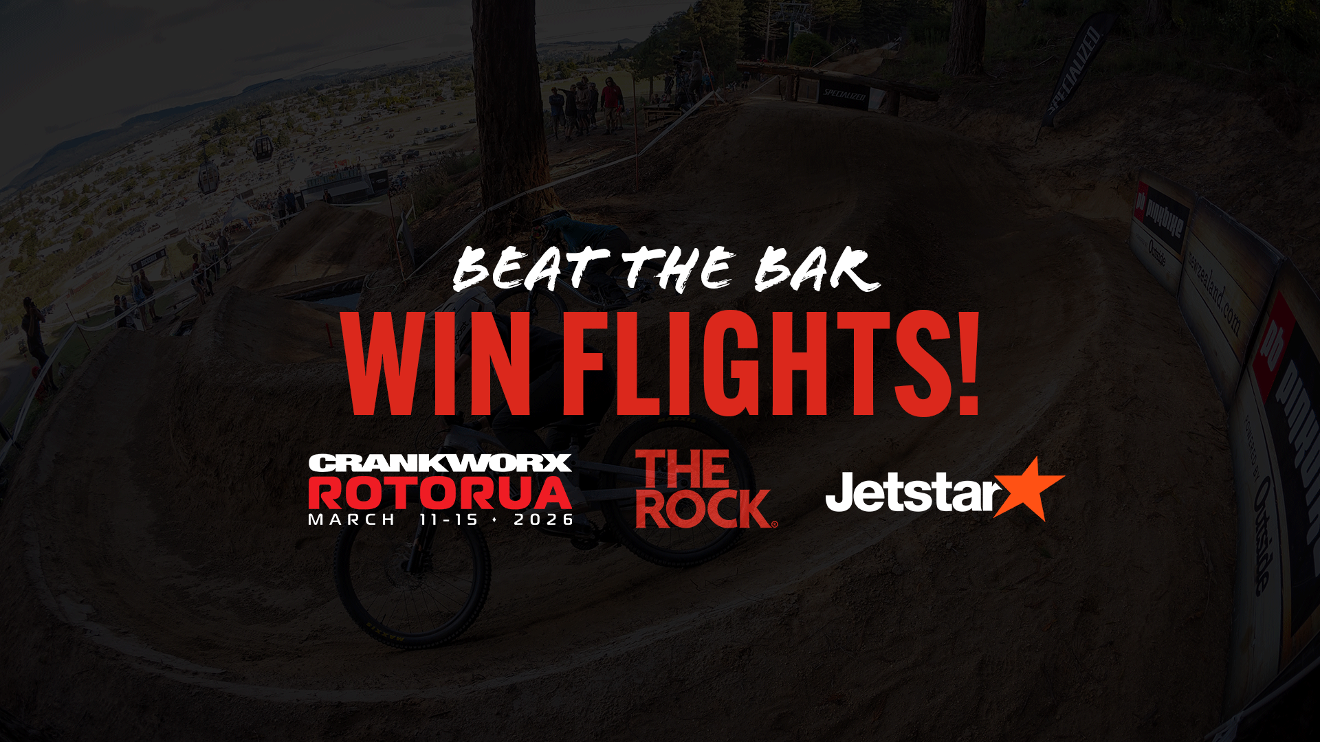A dark mountain biking scene with a blurred biker, featuring overlaid text "BEAT THE BAR WIN FLIGHTS!" and logos for CRANKWORX ROTORUA (March 11-15, 2026), THE ROCK, and Jetstar.