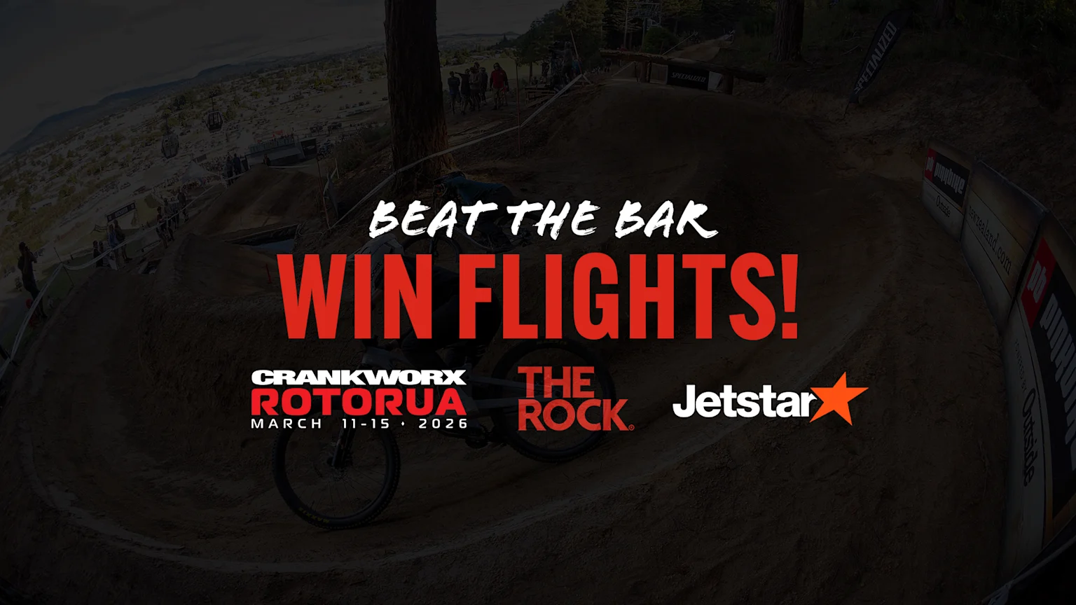 A dark mountain biking scene with a blurred biker, featuring overlaid text "BEAT THE BAR WIN FLIGHTS!" and logos for CRANKWORX ROTORUA (March 11-15, 2026), THE ROCK, and Jetstar.