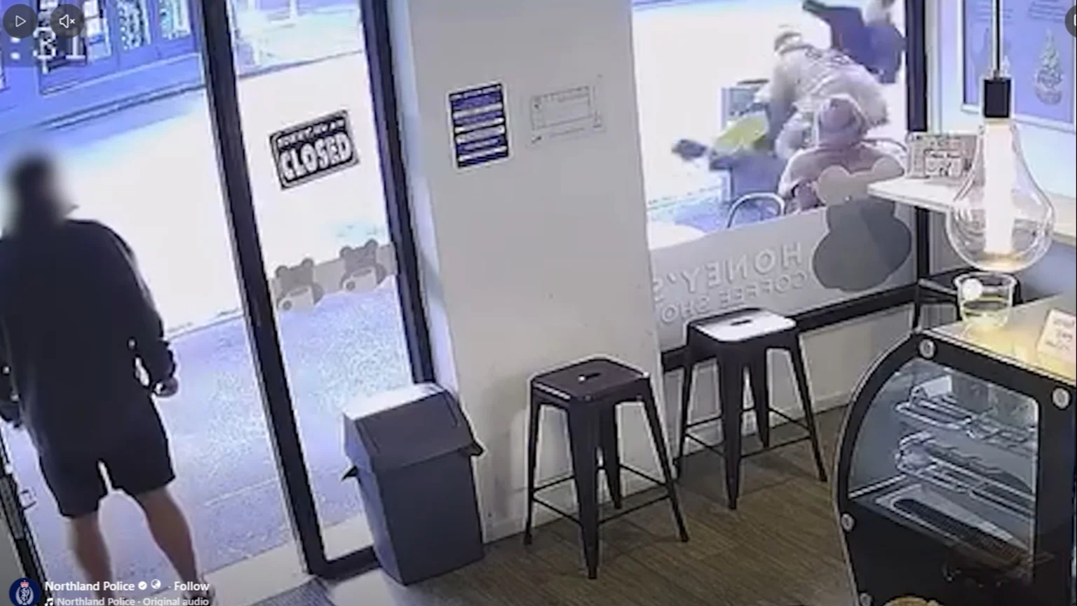 A person stands inside a coffee shop, looking out a glass door with a "CLOSED" sign, towards a blurred struggle involving multiple figures outside.