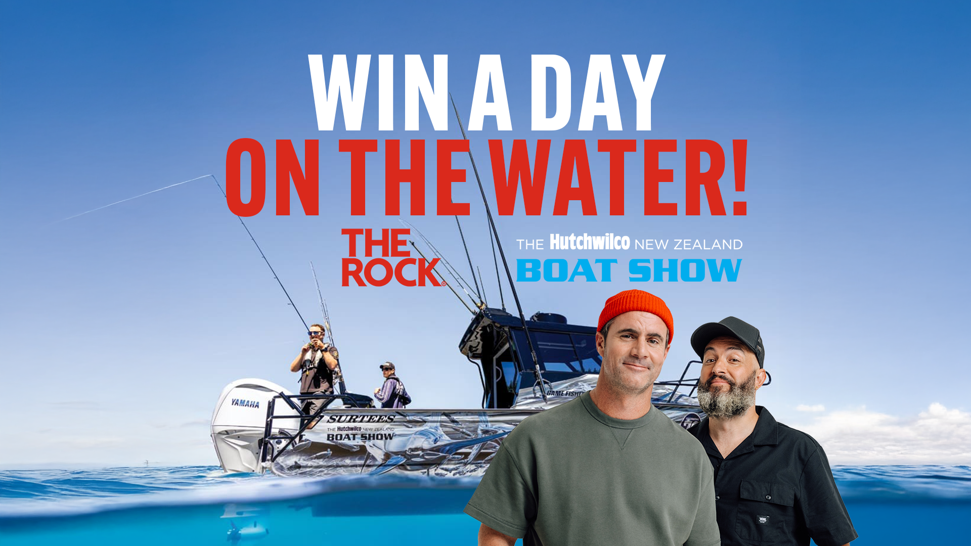 Two smiling men, one wearing an orange beanie, stand partially submerged in water in front of a fishing boat with other men on board, under text that reads "WIN A DAY ON THE WATER!".