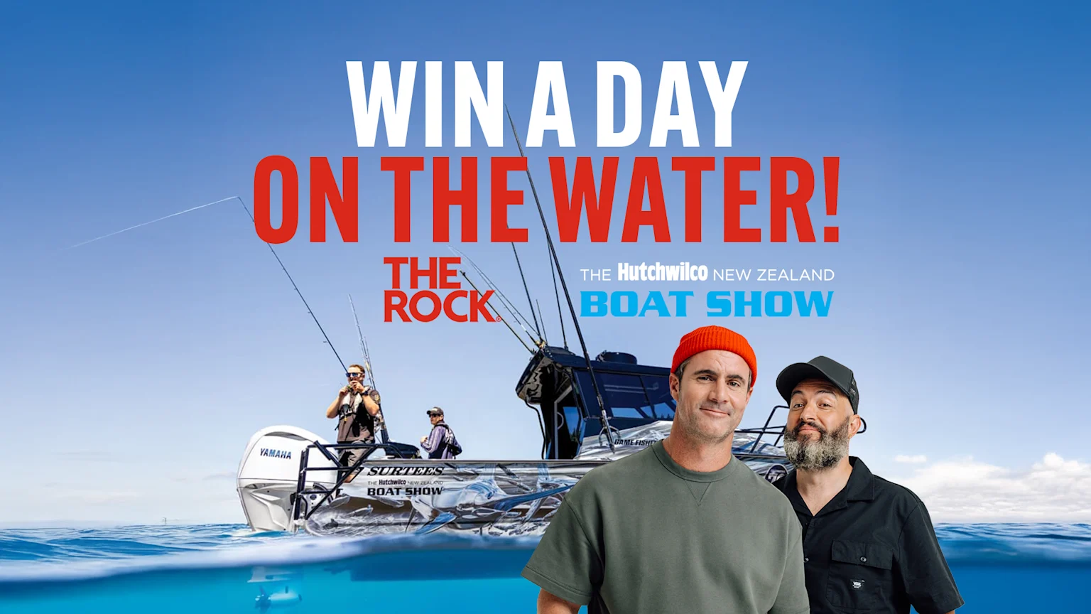 Two smiling men, one wearing an orange beanie, stand partially submerged in water in front of a fishing boat with other men on board, under text that reads "WIN A DAY ON THE WATER!".