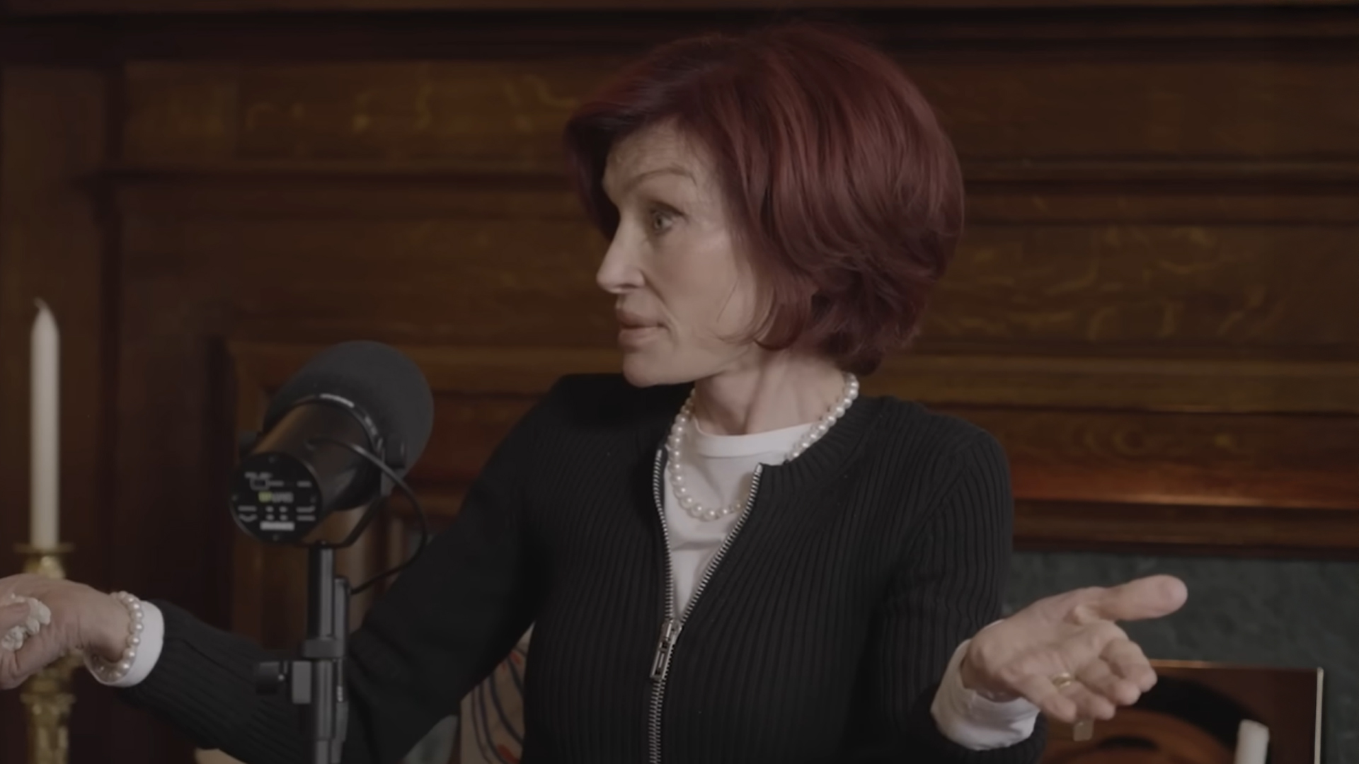 Sharon osbourne sitting at a desk with a microphone, for her podcast The Osbournes