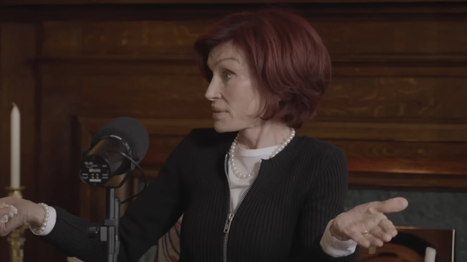 Sharon osbourne sitting at a desk with a microphone, for her podcast The Osbournes
